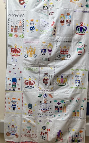 A wall-hanging with rectangles featuring pictures associated with royalty, including crowns, guards in bearskin hats, Big Ben and the Houses of Parliament, the King and Queen, and a Beefeater
