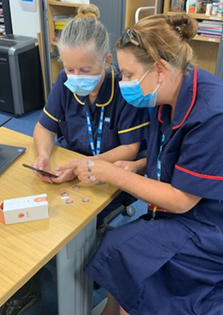 Two nurses conversing at a table over the Julie Merrick (Community Nurse Team Leader) and Katie Fox (Community Wound Care Team Lead) using the Minuteful for Wound app.
