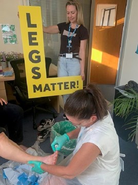 Photo of nurse cleaning a person's feet. Another nurse stands in background with yellow 'Legs Matter!' sign.