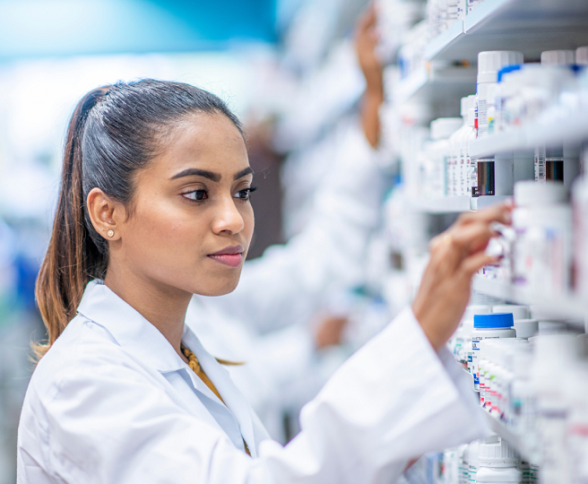 Woman with a pony tail, wearing a white coat looking at medication.