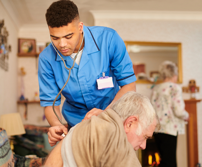 Young man in a light blue tunic listening to patients breathing in their home