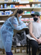 Woman wearing a facemask and plastic gown, giving a young person wearing a cap an injection.