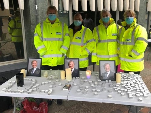 People in yellow hi-vis NHS jackets holding a memorial for MP David Amos